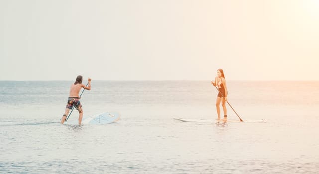 Sea woman and man on sup. Silhouette of happy young woman and man, surfing on SUP board, confident paddling through water surface. Idyllic sunset. Active lifestyle at sea or river