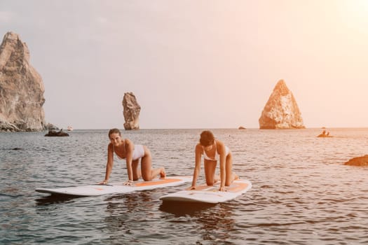 Woman sup yoga. Middle age sporty woman practising yoga pilates on paddle sup surfboard. Female stretching doing workout on sea water. Modern individual hipster outdoor summer sport activity