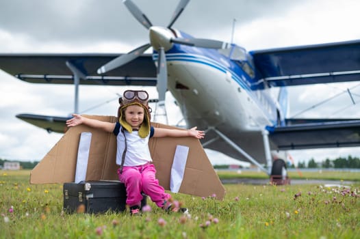 A cute little girl dressed in a cap and glasses of a pilot on the background of an airplane. The child dreams of becoming a pilot