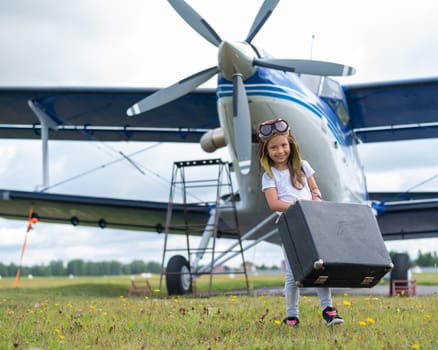 A cute little girl playing on the field by private jet dreaming of becoming a pilot.