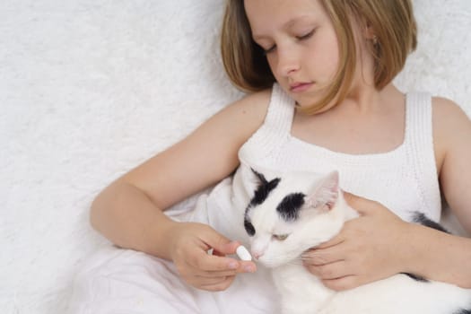 Sick teenage girl feeds a pill to a cat. Medical concept.