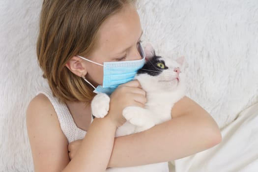 Sick teenage girl in a protective mask hugs a cat. Medical concept.