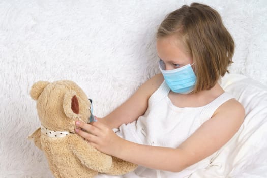 Sick teenage girl puts on a medical protective mask for a toy. Medical concept.