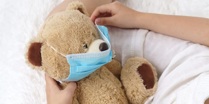 Sick teenage girl puts on a medical protective mask for a toy. Medical concept.