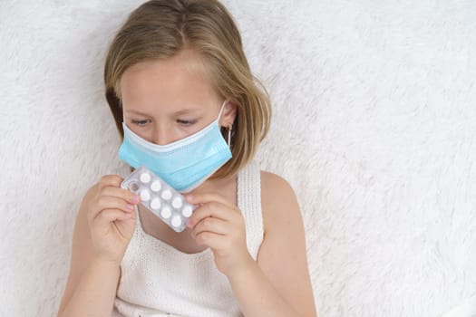 A sick teenage girl in a protective mask squeezes pills out of a package. Medical concept.