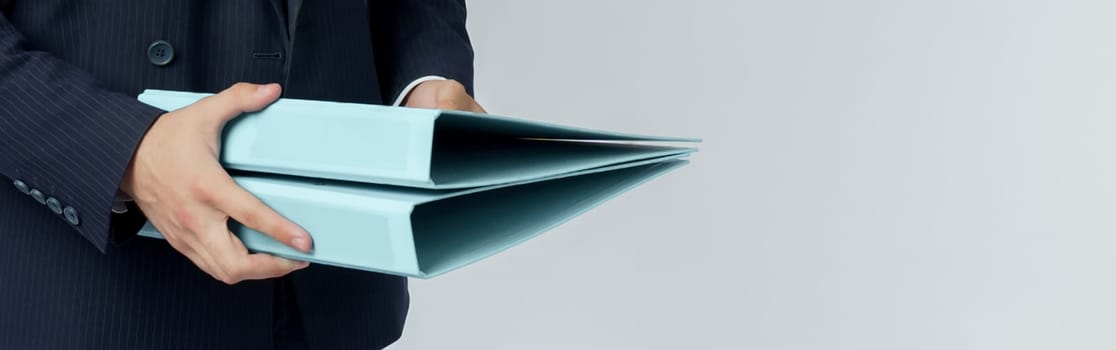 Businessman in a blue suit holds a folder in his hands on a white background. No face visible.