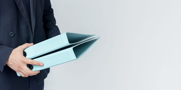 Businessman in a blue suit holds a folder in his hands on a white background. No face visible.