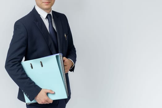Businessman in a blue suit holds a folder in his hands on a white background. No face visible.
