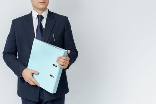 Businessman in a blue suit holds a folder in his hands on a white background. No face visible.