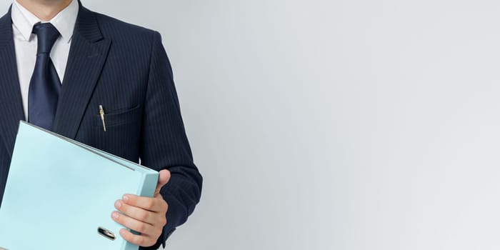 Businessman in a blue suit holds a folder in his hands on a white background. No face visible.