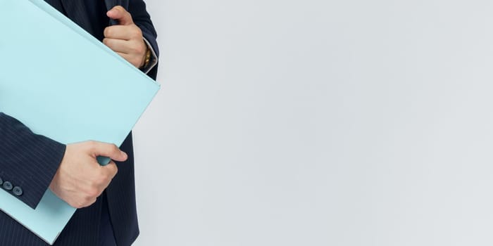 Businessman in a blue suit holds a folder in his hands on a white background. No face visible.