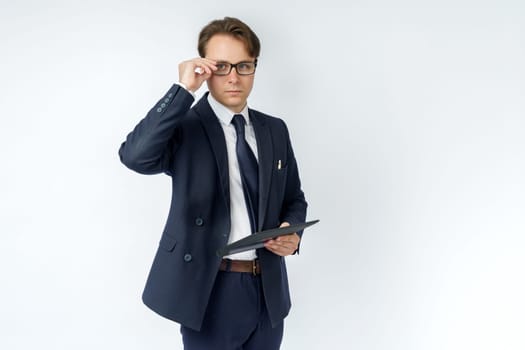 Portrait of a businessman in a blue suit who is holding an electronic tablet in his hands and adjusting his glasses. White background. Business and finance concept