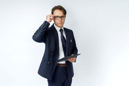 Portrait of a businessman in a blue suit who is holding an electronic tablet in his hands and adjusting his glasses. White background. Business and finance concept