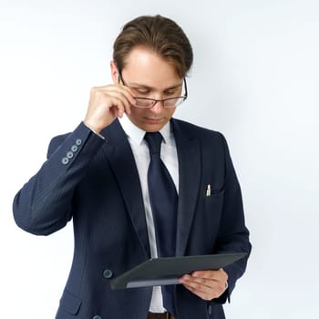 Portrait of a businessman in a blue suit who is holding an electronic tablet in his hands and adjusting his glasses. White background. Business and finance concept