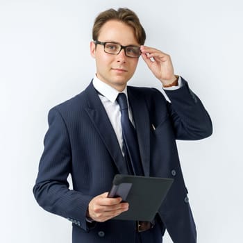 Portrait of a businessman in a blue suit who is holding an electronic tablet in his hands and adjusting his glasses. White background. Business and finance concept