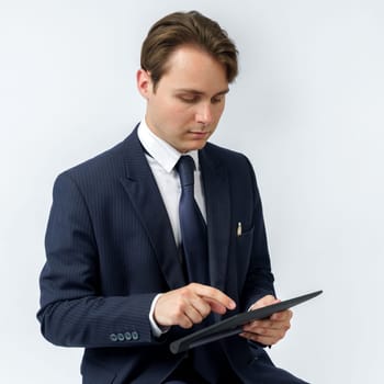 Portrait of a businessman in a blue suit who sits and works with an electronic tablet. White background. Business and finance concept