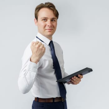 Portrait of a businessman raised his hand clenched into a fist, in the other hand an electronic tablet. White background. Business and finance concept