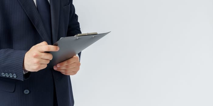 Businessman in a blue suit holds a folder in his hands on a white background. No face visible.