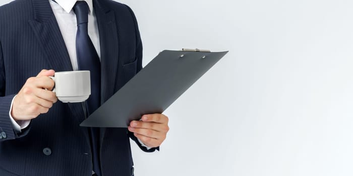 Businessman holds a cup of coffee and a tablet in his hands. White background. No face visible. Business and finance concept