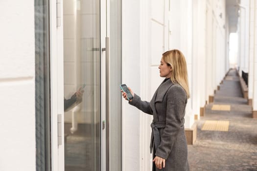 Young stylish woman getting access to the building by attaching smartphone to intercom. Concept of modern security technologies for access and smart home.