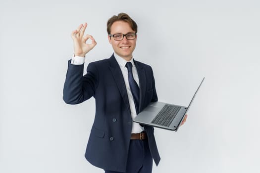 A businessman is holding a laptop, his other hand is showing OK gesture. White background. Business and finance concept