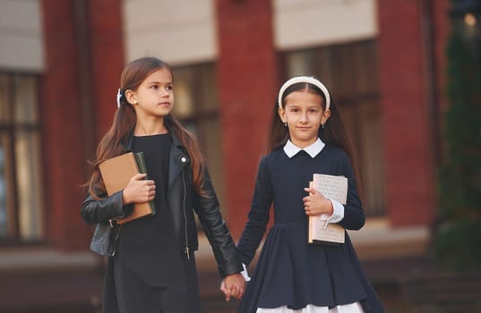 Walking together. Two schoolgirls is outside near school building.