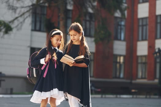 Walking together. Two schoolgirls is outside near school building.