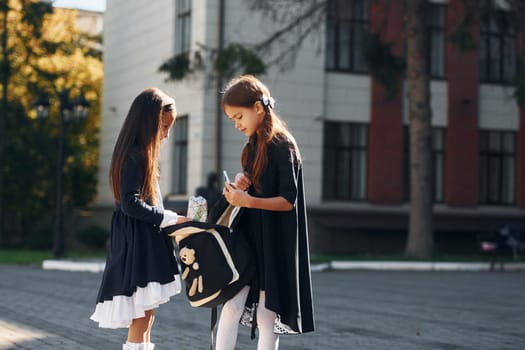 Walking together. Two schoolgirls is outside near school building.
