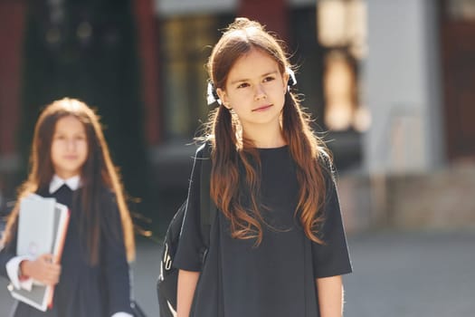 Walking together. Two schoolgirls is outside near school building.