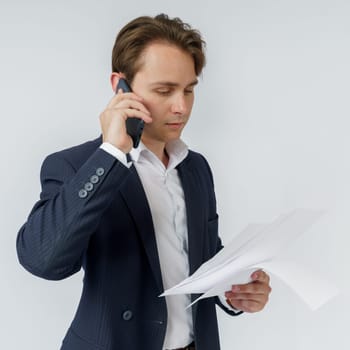 Portrait of a businessman who is talking on the phone and reading documents. White background.