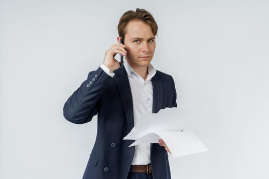 Portrait of a businessman who is talking on the phone and reading documents. White background.