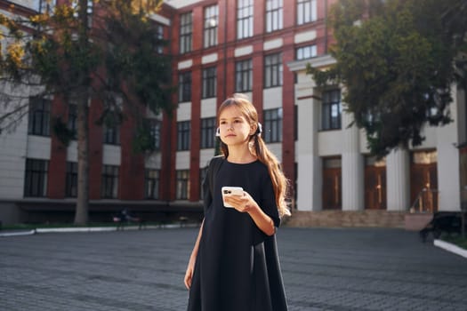 In black uniform. Schoolgirl is outside near school building.