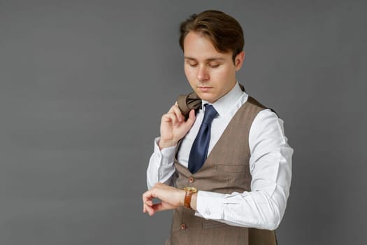 Portrait of a businessman who looks at his watch and holds a jacket over his shoulder. Gray background. Business and finance concept