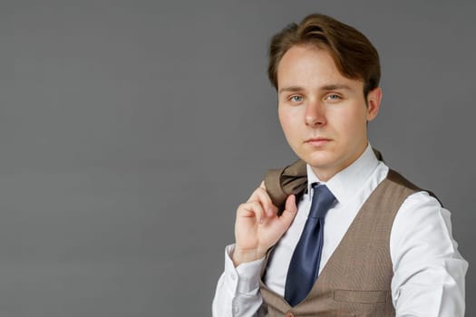 Portrait of a businessman who looks into the camera and holds a jacket over his shoulder. Gray background. Business and finance concept