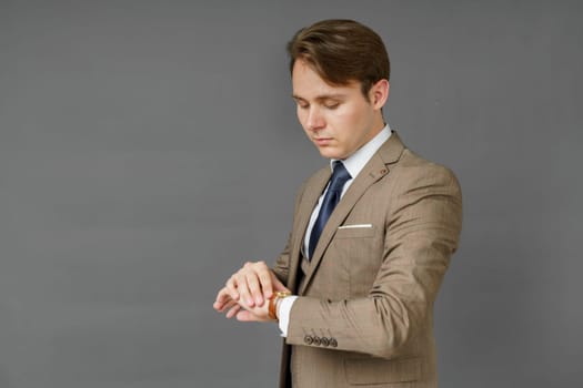 Portrait of a businessman who looks at his watch and holds a jacket over his shoulder. Gray background. Business and finance concept