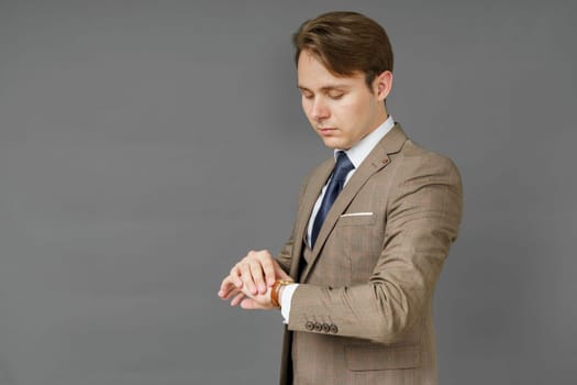 Portrait of a businessman who looks at his watch and holds a jacket over his shoulder. Gray background. Business and finance concept