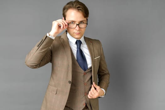 Portrait of a businessman in a suit looking at the camera and adjusting his glasses. Gray background. Business and finance concept