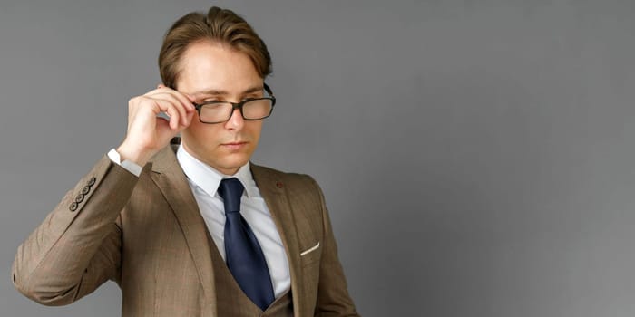Portrait of a businessman in a suit, who adjusts his glasses. Gray background. Business and finance concept