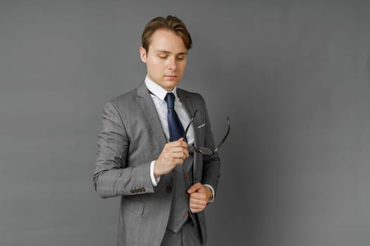 Portrait of a businessman in a suit, who adjusts his glasses. Gray background. Business and finance concept