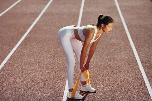 Doing stretching by using tape. Young woman in sportive clothes is exercising outdoors.