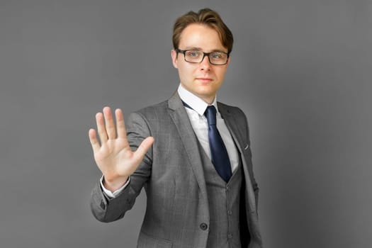 Portrait of a businessman in a suit who stretches out his hand in front of his palm. Stop. Gray background. Business and finance concept