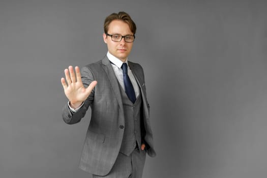 Portrait of a businessman in a suit who stretches out his hand in front of his palm. Stop. Gray background. Business and finance concept