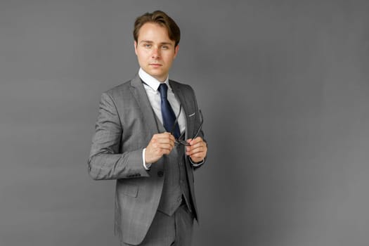 Portrait of a businessman in a suit, who adjusts his glasses. Gray background. Business and finance concept