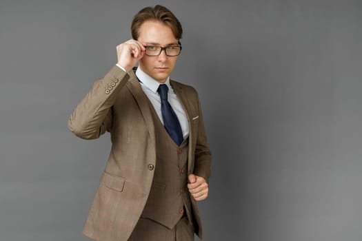 Portrait of a businessman in a suit, who adjusts his glasses. Gray background. Business and finance concept