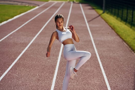 On the running track. Young woman in sportive clothes is exercising outdoors.