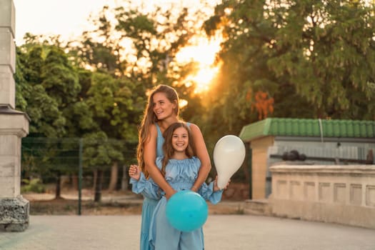 Mother daughter sunset. in blue dresses with flowing long hair against the backdrop of sunset. The woman hugs and presses the girl to her. They are looking at the camera