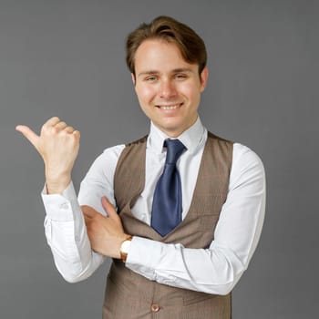 An emotional portrait of a businessman who shows a gesture of his hand to the right. Gray background. Business and finance concept