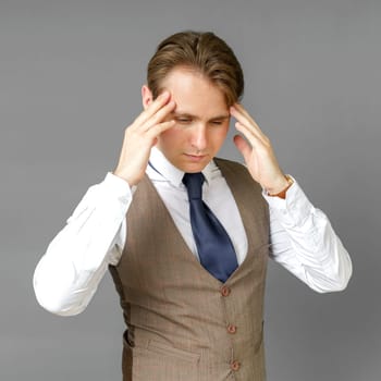 An emotional portrait of a businessman who touches his head with his hands. Gray background. Business and finance concept