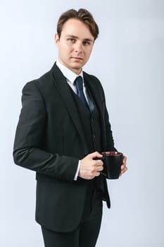Business and finance concept. A man in a black suit holds a cup of coffee in his hands. Light background