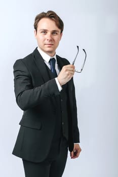 Business and finance concept. A man in a black suit holds glasses in his hands. Light background